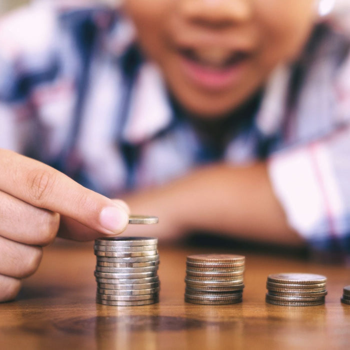 Close up on student hands counting coins and stacking them. They have an open mouth smiling facial expression showing interest.