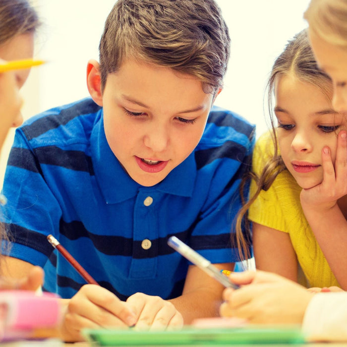 A group of four young children is gathered closely together, actively working on a collaborative task at a table, with focused expressions as they share ideas and write in a notebook.