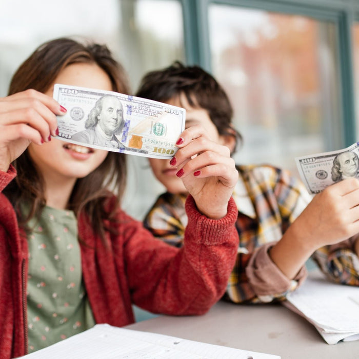 2 students sitting at a desk with notebooks and looking up close at money bills, 